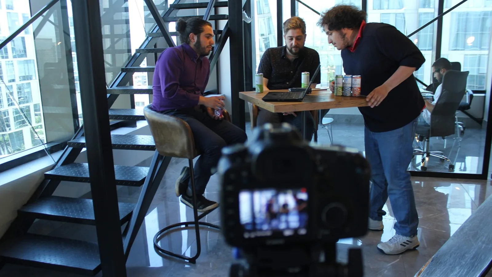 Ein Filmteam bespricht während der Vorbereitung eines Drehs die Planung am Laptop, im Vordergrund eine Kamera auf einem Stativ.