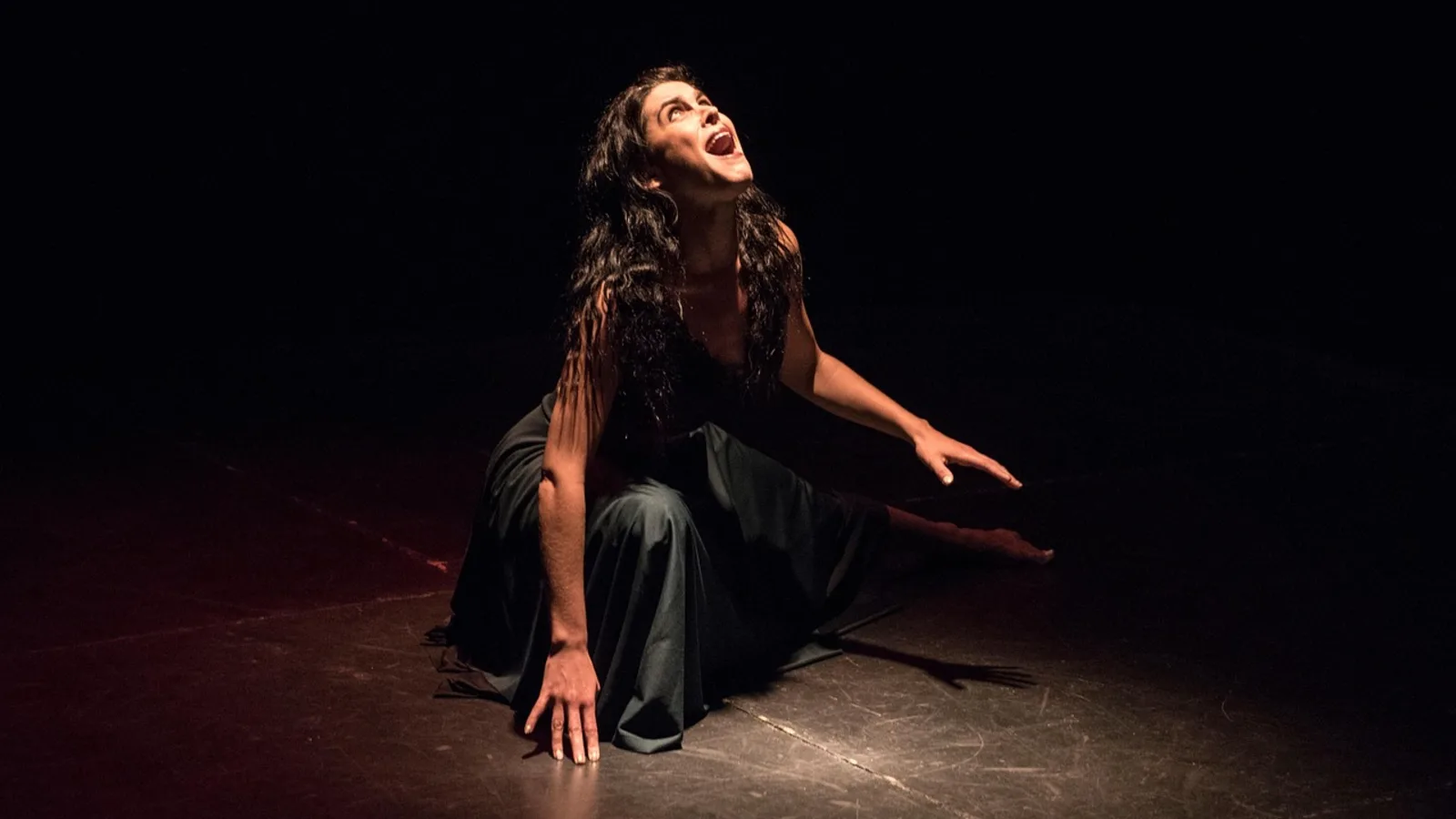 Eine Schauspielerin bei einer intensiven Performance auf einer dunklen Bühne im Scheinwerferlicht.