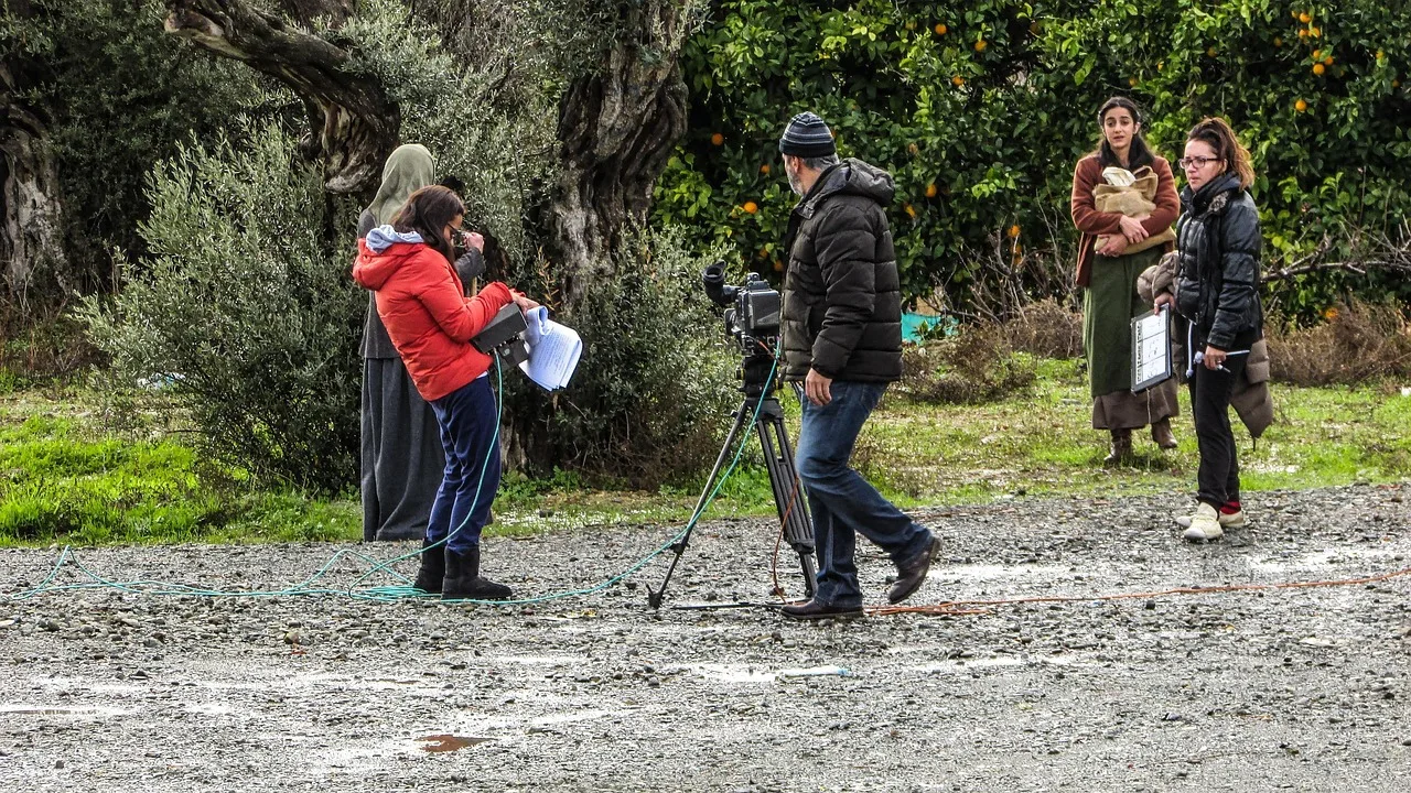 Filmcrew dreht mit Stativkamera an einem realen Drehort im Freien, umgeben von natürlichem Licht und unebenem Gelände.